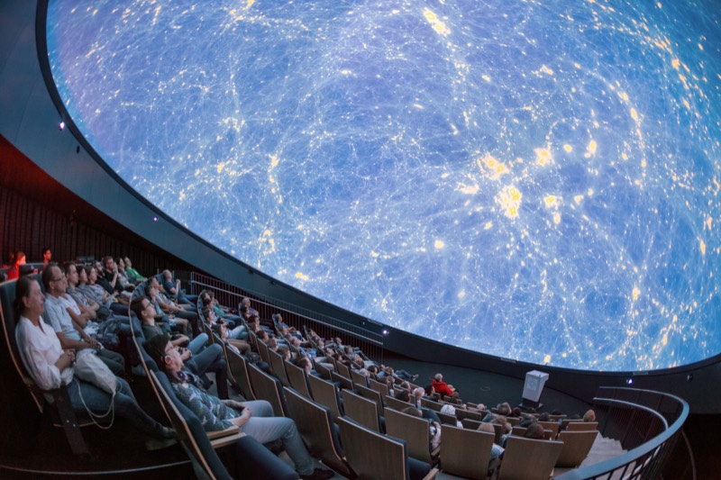 An audience looking up at a planetarium dome full of stars