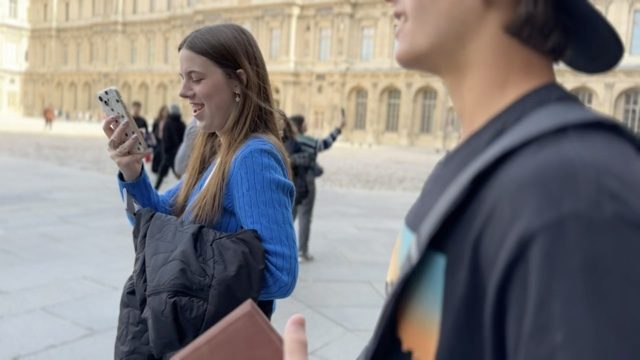 A GoXL student laughing at her phone in the Louvre courtyard